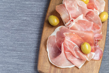 Prosciutto ham with green olives on wooden board, horizontal, copy space
