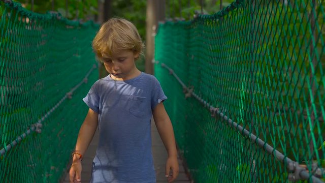 Steadicam shot of a kute little boy having fun on the hanging suspension bridge in the Eco Park in the Kuala Lumpur city