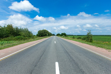 road through the green field and clouds on blue sky in summer day