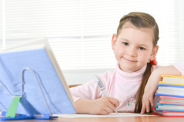Cute schoolgirl sitting at table and doing homework at home
