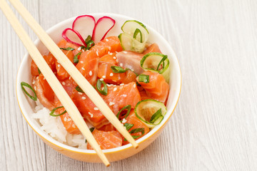 Hawaiian poke with salmon and sesame seeds, boiled rice, fresh cucumber, radish and green onions in glass bowl