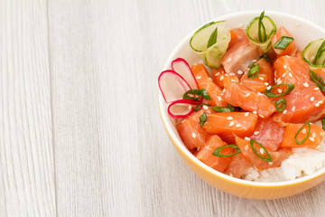 Hawaiian poke with salmon and sesame seeds, boiled rice, fresh cucumber, radish and green onions in glass bowl