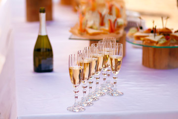 on a white table a bottle of champagne and 7 glasses, as well as food