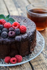 Homemade chocolate cake decorated with black and red raspberries on glass plate with cup of tea