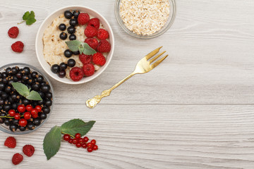 Oatmeal porridge in porcelain bowl with currant berries and raspberries, decorated with mint leaves