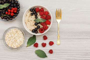 Oatmeal porridge in porcelain bowl with currant berries and raspberries, decorated with mint leaves