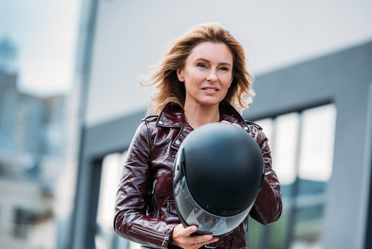 Beautiful Woman In Leather Jacket Holding Motorcycle Helmet On Street And Looking Away