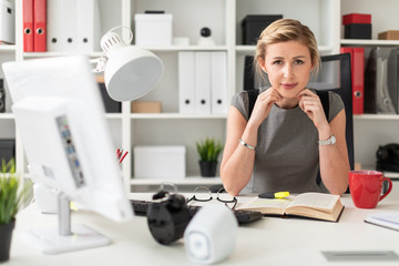 A young girl is sitting at a table in the office. Before the girl lies an open book.