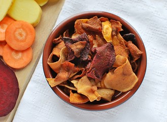 Vegetable chips in rustic bowl and fresh carrots, beetroot and potatoes.Healthy vegan food.
