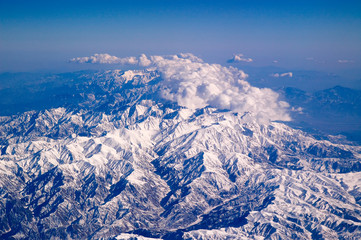 Fototapeta premium Mountains covered with snow and clouds, aerial view. Earth planet surface. Travelling around world. Environment protection and ecology. I take my earth with a little blue sky