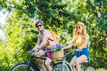 Naklejka premium happy couple riding retro bicycles in park on summer day