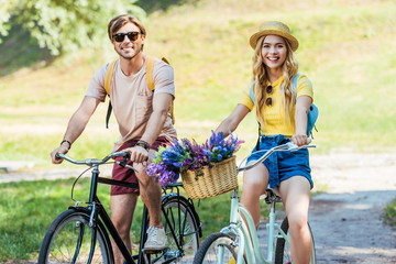 Naklejka premium happy couple riding retro bicycles in park on summer day