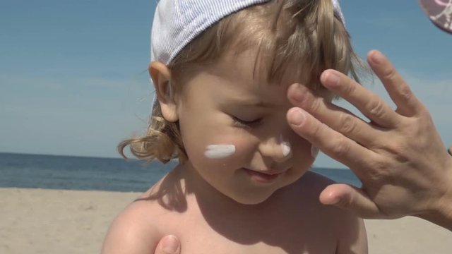 Sun protection. Mother anoints her son face protective cream on the beach. Family vacation at the sea. Slow motion.  Portrait of little boy in suncream