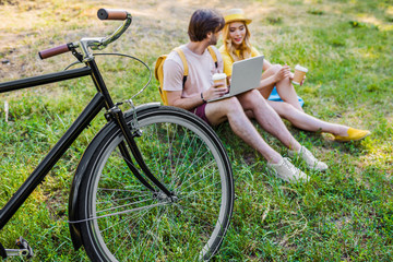 Obraz premium young couple with coffee to go using laptop in park