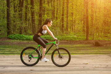 Fototapeta na wymiar Young woman in a sport bike suit with a bicycle in the park. Health and relaxation.