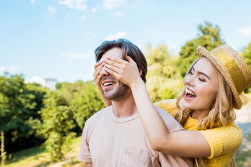 side view of happy woman covering boyfriends eyes in park on summer day