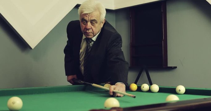 An old gray-haired man plays billiards.