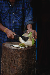 A man is cutting a fresh young green coconut with a sharp chopper or aruval for tourists
