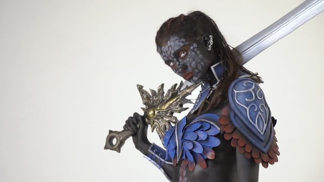 Pompous woman dark warrior in body art stands with a huge sword and looks at the camera, slow motion