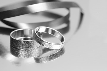 Two wedding rings with reflection with silver ribbon on grey background with copy space.
