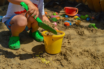 the child is playing in the sandbox.  around are scattered various toys and tools for construction