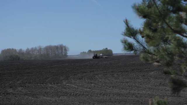 Tractor rides a plowed field and sows grain