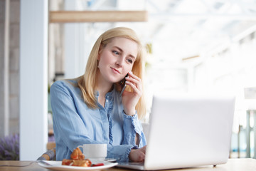 Pretty young woman outsourcing employee of large company working remotely sitting at table in cafe...