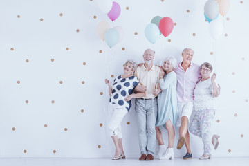 Group of enthusiastic elderly people with colorful balloons have fun during meeting