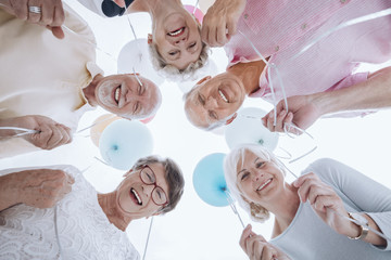 Low angle of happy senior people in the circle with balloons during party