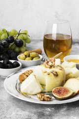 Snacks with wine - various types of cheeses, figs, nuts, honey, grapes on a gray background