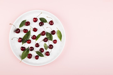 Ripe cherry and green leaves on a pink background. Top view, copy space. Food background