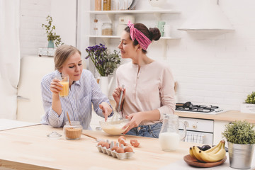 Two cheerful friends cook together desserts and gossip in the kitchen