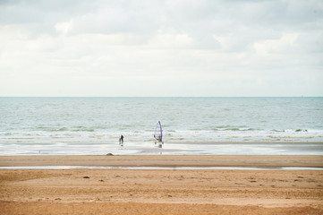 Surfing on the beach in front of waves at autumn with some people walking by