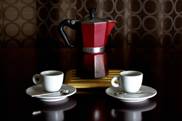 Moka stove-top espresso coffee maker with cups and spoons in a variety of dramatic lighting on a wooden table at night.