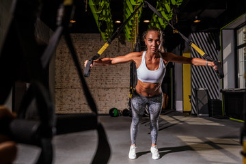 Attractive female fitness coach performing Chest Press - TRX exercise