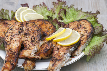 Fried salmon on a white plate decorated with lemon and salad