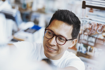 Young atrractive spectacled man choosing book on a book shelf.
