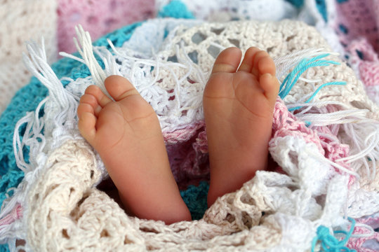 2 Weeks Old Newborn Baby Feet In Soft Knitted Colorful Blanket
