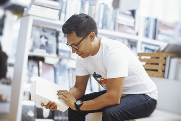 Young spectacled brunette man sitting and reading book with blank cover.