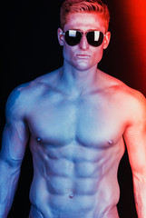 Male sunglasses & body concept. Portrait of a handsome muscular male model in trendy sunglasses posing over black background. Studio shot