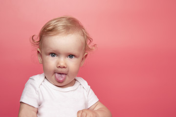 baby girl shows tongue on pink background. little girl makes an appearance