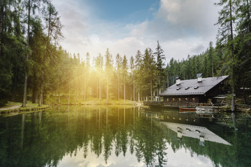 Fototapeta premium See im Wald mit Hütte bei Sonnenuntergang mit Tannenbäumen