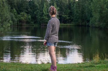 Fototapeta na wymiar Young woman look at the pond on the background of the forest in the countryside