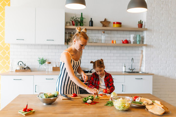 Photo of beautiful woman with her daughter cutting vegetables in kitchen
