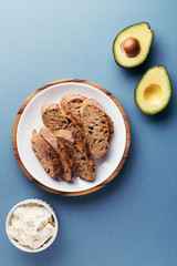 Bruschetta with cream cheese and avocado, french chopped baguette on the plate and avocado on blue background. Top view.