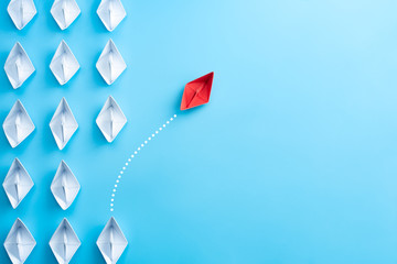 Group of white paper ship in one direction and one red paper ship pointing in different way on blue background. Business for innovative solution concept. - obrazy, fototapety, plakaty