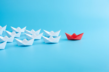 Leadership concept with red paper ship leading among white on blue background.