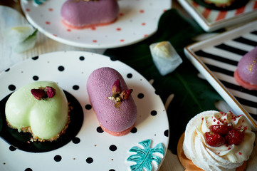Moscovie cakes purple and lemon yellow. Pistachio and fruit. Meringue Anna Pavlova . Culinary art. On striped graphic saucers