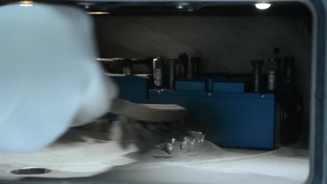 A man in gloves cleans the working chamber with a brush from a metal powder. 3D printer printing metal. Laser sintering machine for metal. Metal is sintered under action of laser into shape in chamber