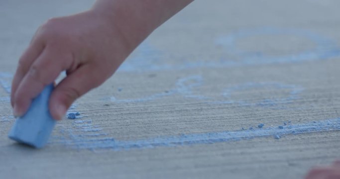 Toddler drawing lines on sidewalk with blue chaulk - close up